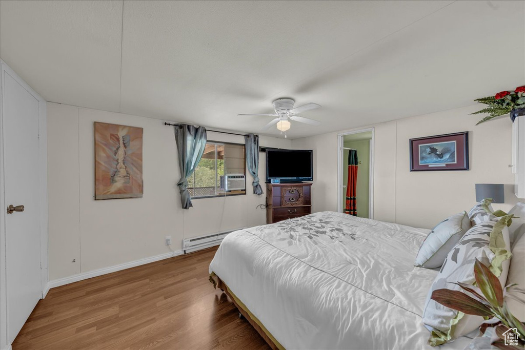 Bedroom with wood finished floors, a baseboard radiator, cooling unit, baseboards, and ceiling fan
