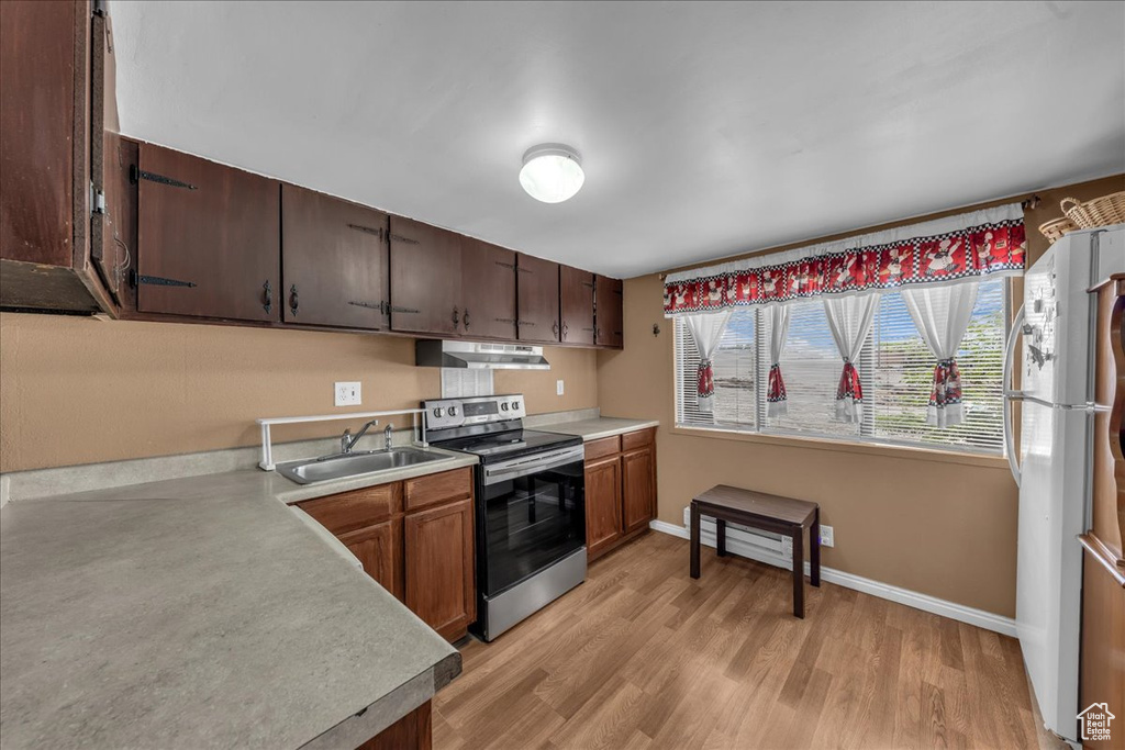 Kitchen featuring electric range, a sink, under cabinet range hood, freestanding refrigerator, and light countertops