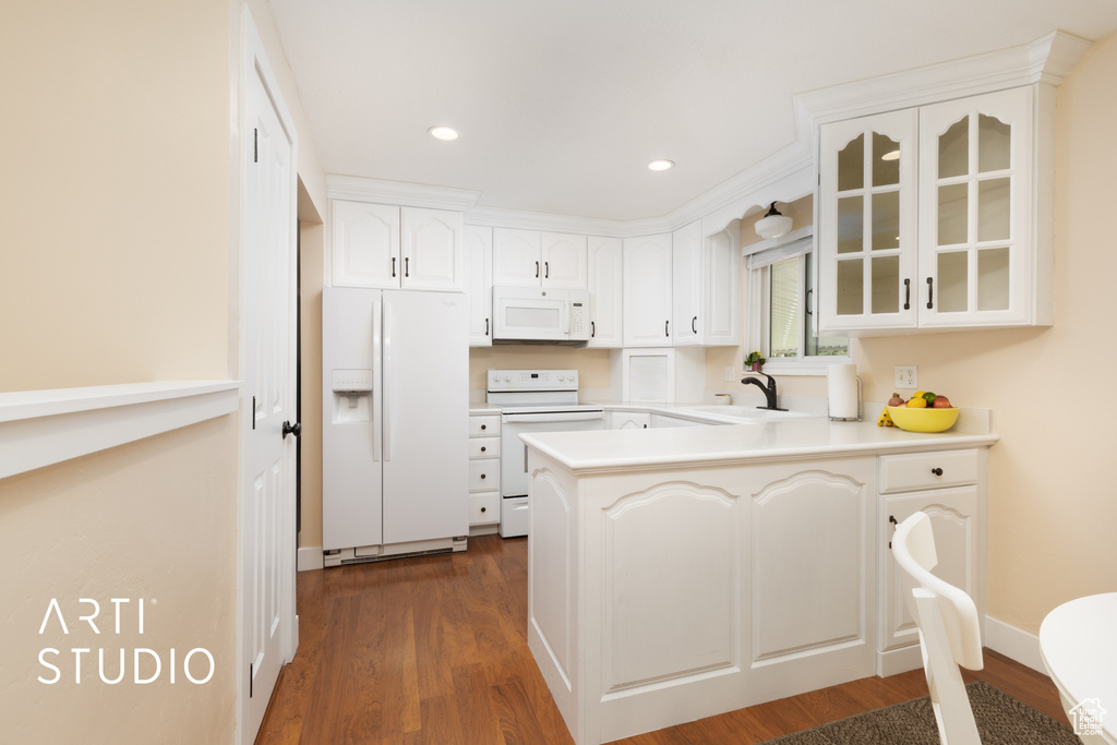 Kitchen featuring white appliances, a peninsula, glass insert cabinets, dark wood finished floors, and a sink