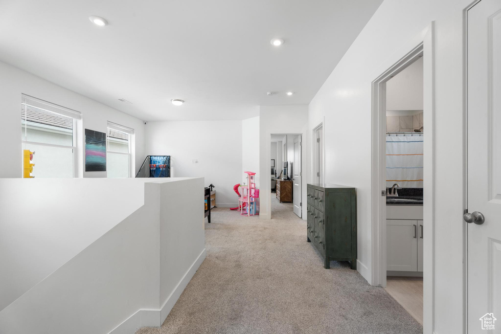 Hallway featuring an upstairs landing, light carpet, a sink, recessed lighting, and baseboards