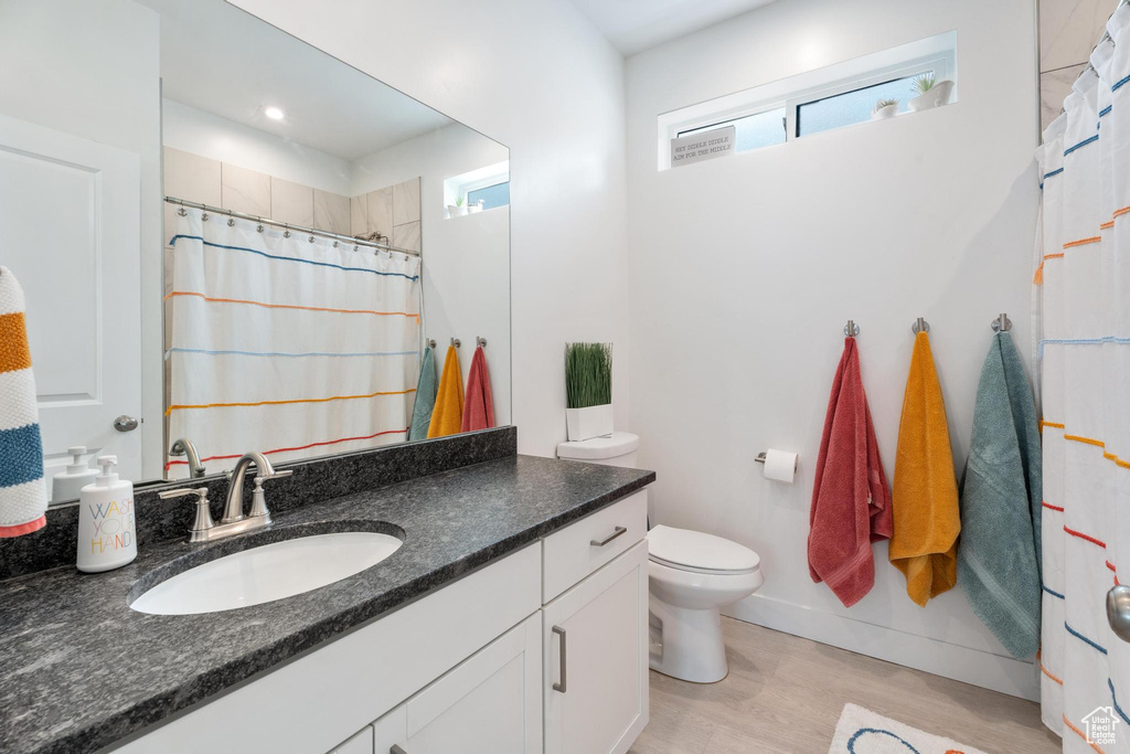 Full bath with wood finished floors, vanity, toilet, curtained shower, and baseboards