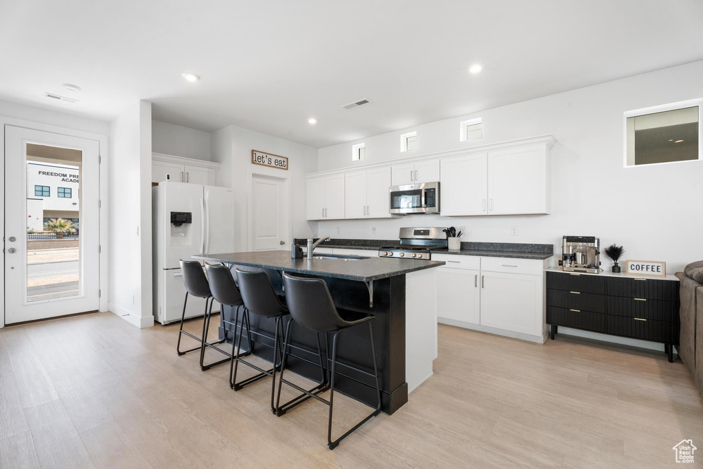 Kitchen with appliances with stainless steel finishes, a breakfast bar area, light wood finished floors, white cabinetry, and recessed lighting