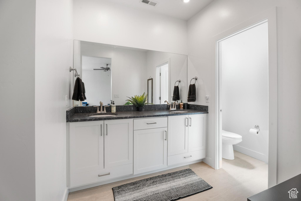 Bathroom with toilet, double vanity, wood finished floors, baseboards, and a ceiling fan