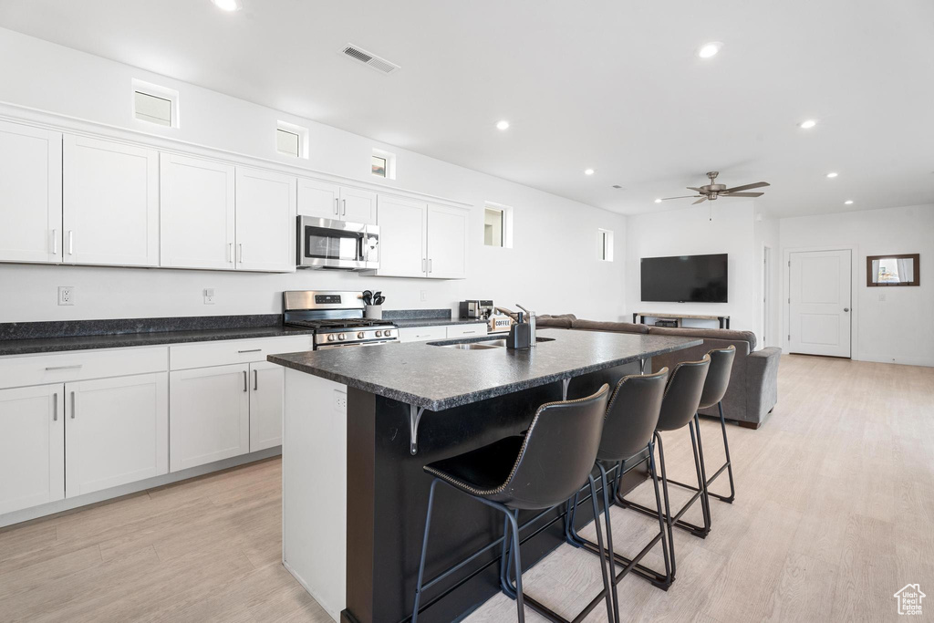 Kitchen featuring appliances with stainless steel finishes, light wood finished floors, a kitchen bar, recessed lighting, and an island with sink