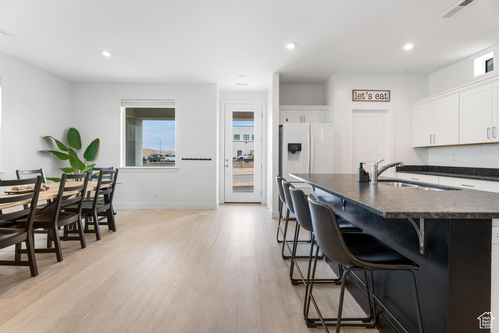 Kitchen featuring dark countertops, a sink, light wood finished floors, a kitchen bar, and white cabinetry