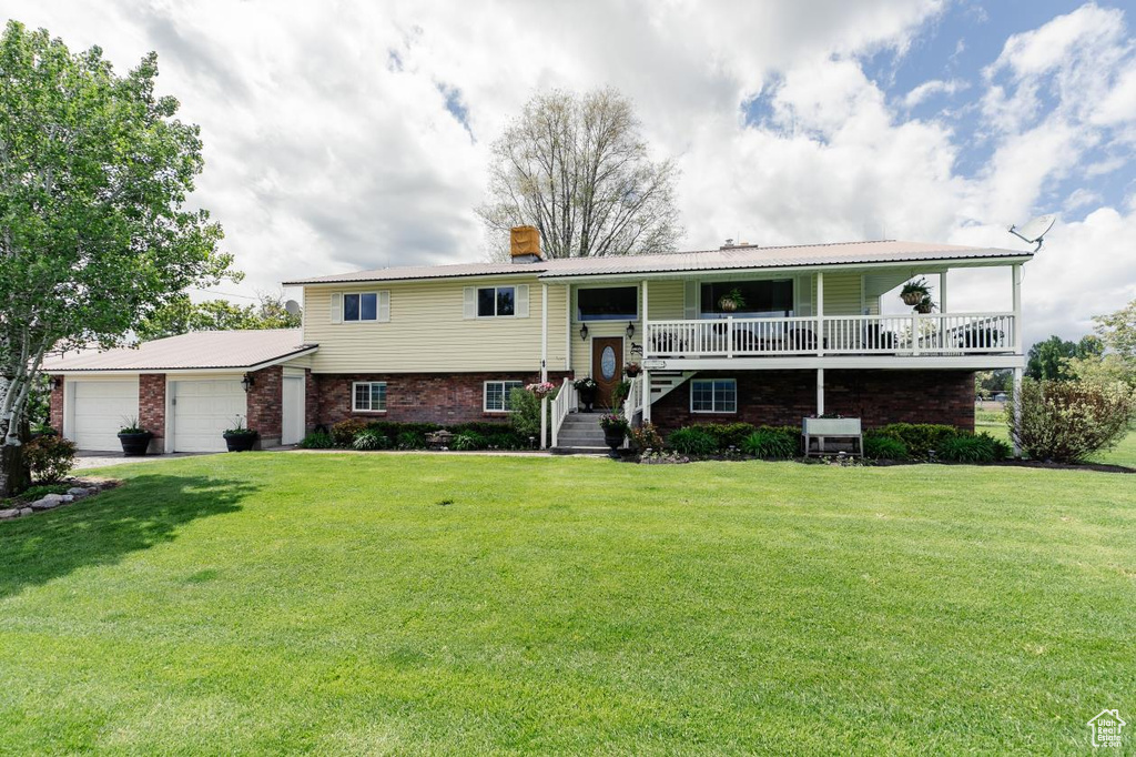 Bi-level home featuring an attached garage, a chimney, a front lawn, brick siding, and metal roof