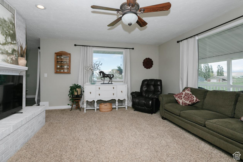Carpeted living area featuring ceiling fan, baseboards, and a brick fireplace