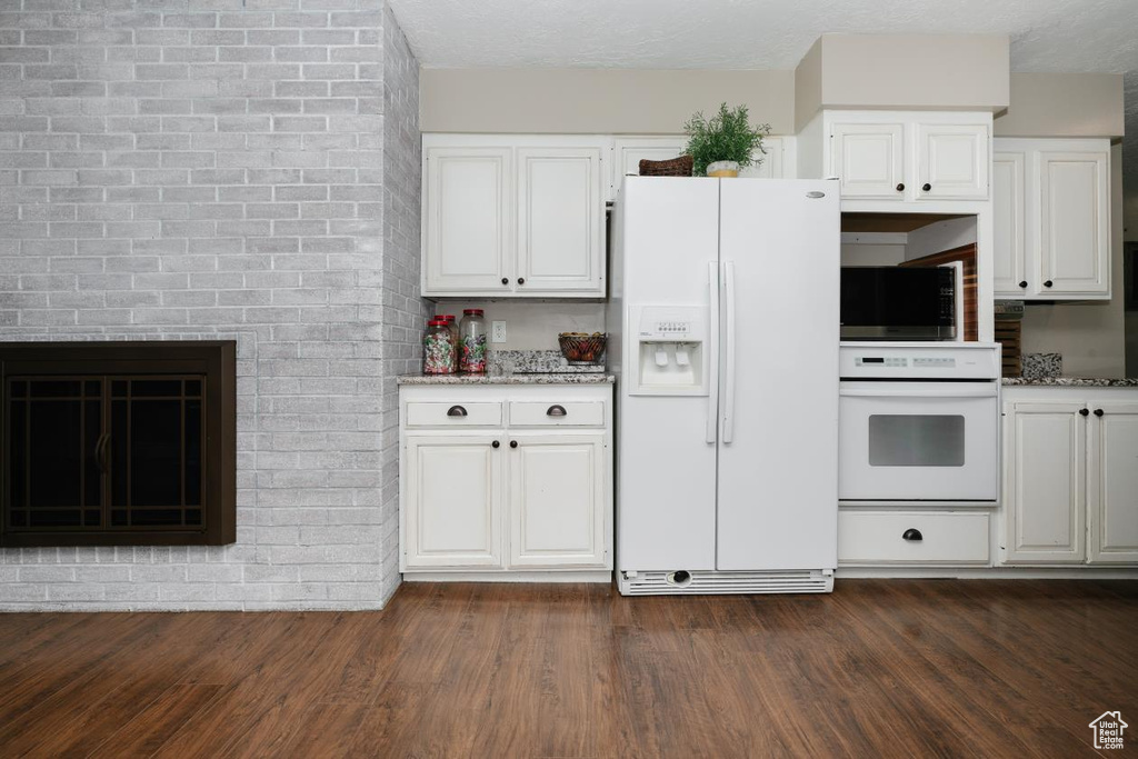 Kitchen featuring white appliances, white cabinetry, dark wood-style flooring, and light stone countertops