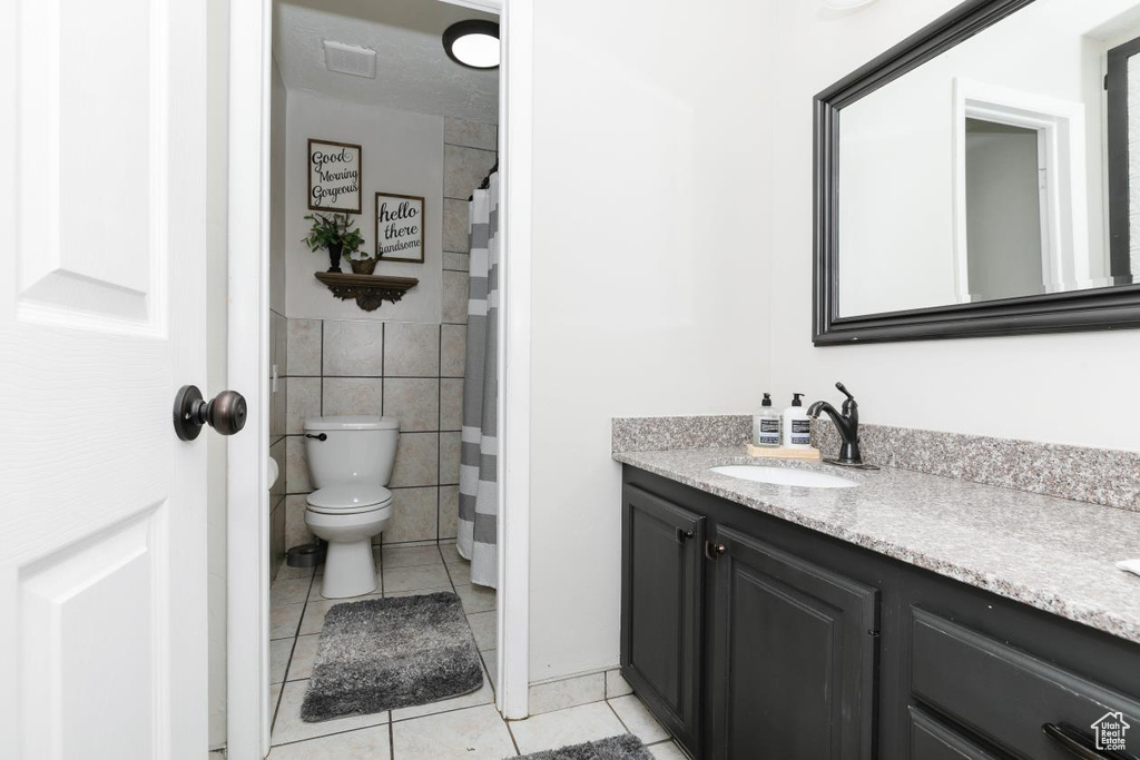 Bathroom featuring tile patterned flooring, vanity, toilet, and tile walls