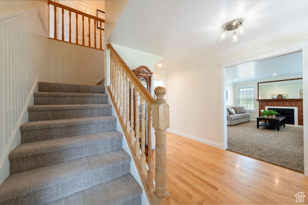 Staircase with wood finished floors, baseboards, a fireplace, and ornamental molding