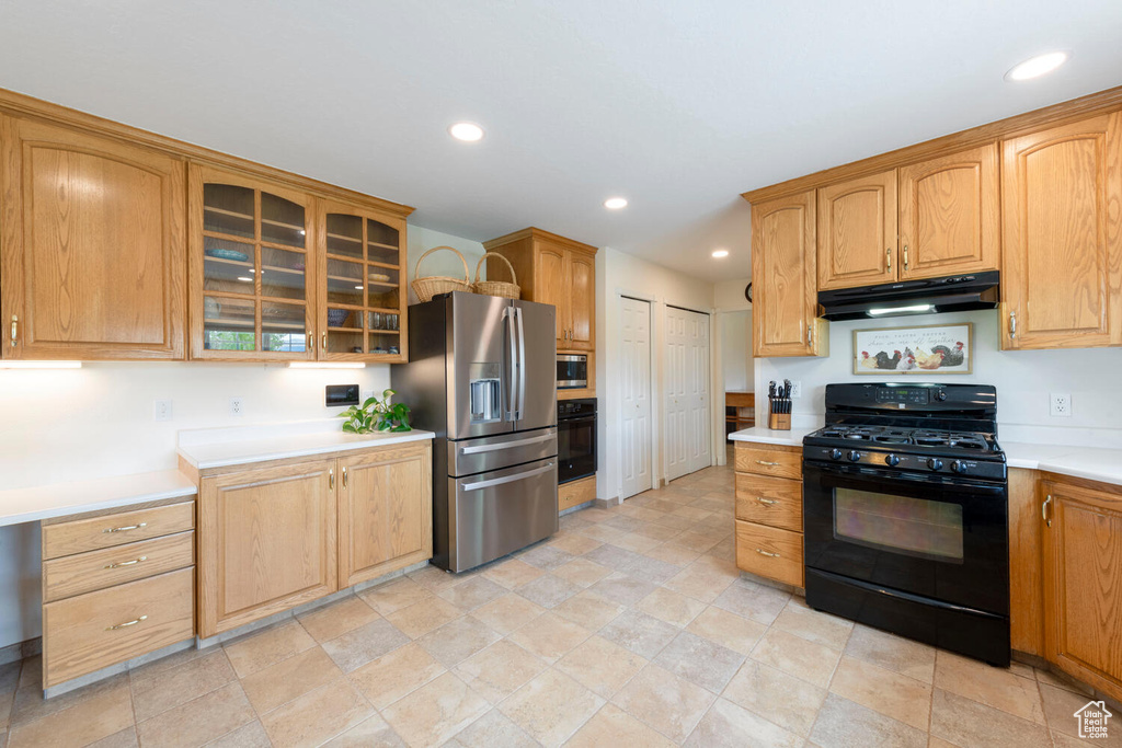 Kitchen with black appliances, under cabinet range hood, light countertops, glass insert cabinets, and recessed lighting