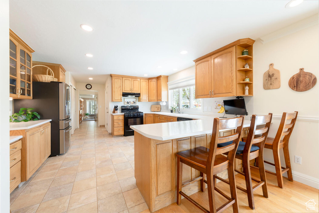 Kitchen featuring gas stove, under cabinet range hood, a peninsula, glass insert cabinets, and light countertops
