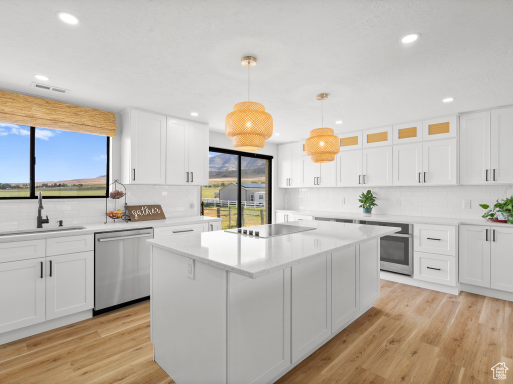 Kitchen with stainless steel appliances, a sink, decorative backsplash, white cabinets, and a center island