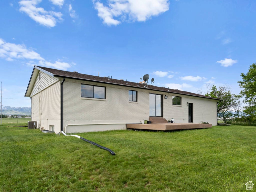 Rear view of house featuring brick siding, cooling unit, and a lawn