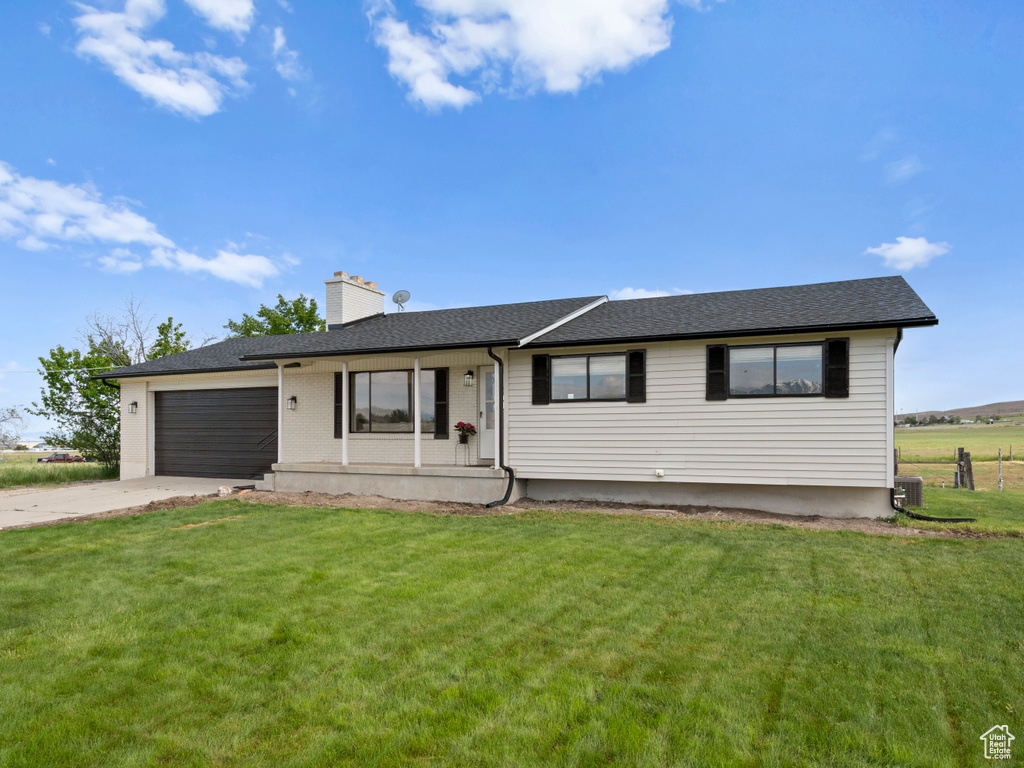 Ranch-style home featuring an attached garage, a chimney, a front lawn, concrete driveway, and central AC unit