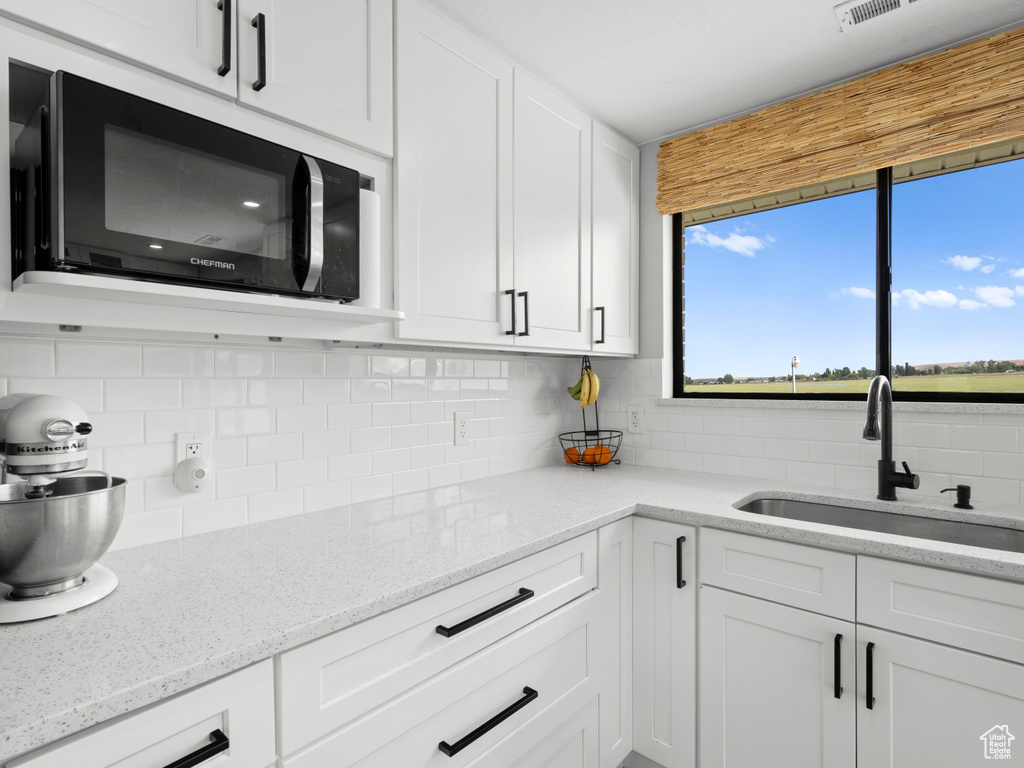 Kitchen featuring a sink, decorative backsplash, white cabinetry, and light stone countertops