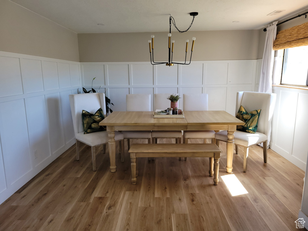 Dining space with a decorative wall, a chandelier, light wood finished floors, and wainscoting