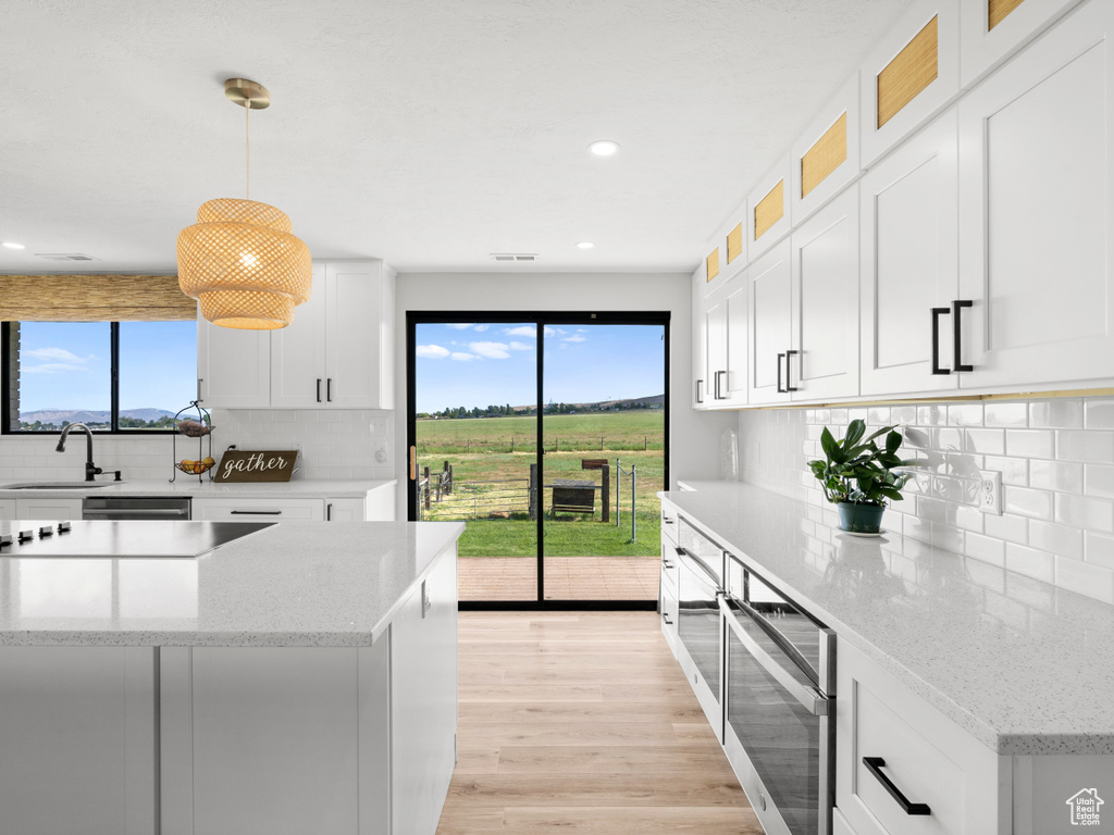 Kitchen featuring a sink, backsplash, light wood-style floors, white cabinets, and light stone counters