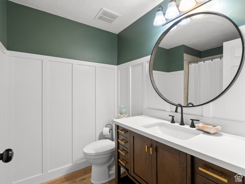 Full bath with wood finished floors, toilet, vanity, a wainscoted wall, and a decorative wall