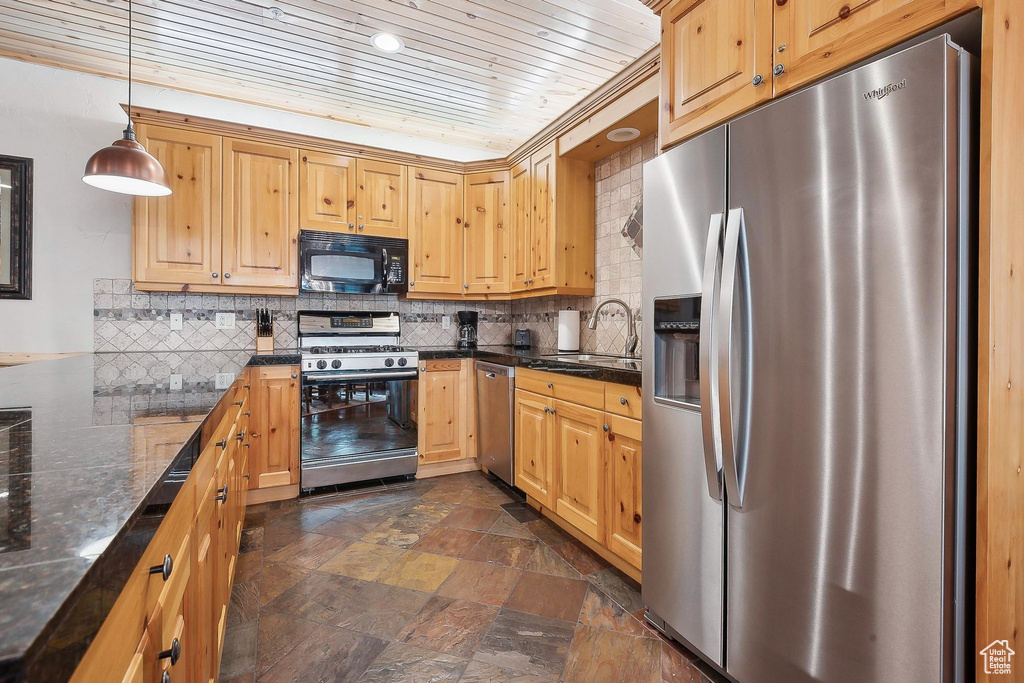 Kitchen featuring stainless steel appliances, a sink, dark stone finish floors, decorative backsplash, and wooden ceiling