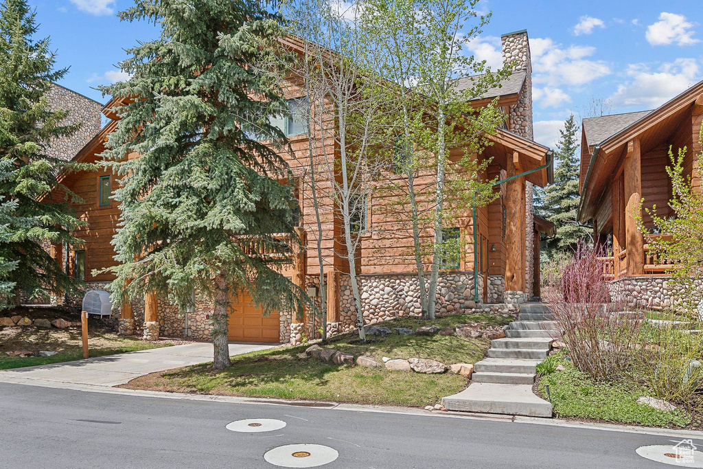 View of front of property featuring stone siding, concrete driveway, a garage, and a chimney