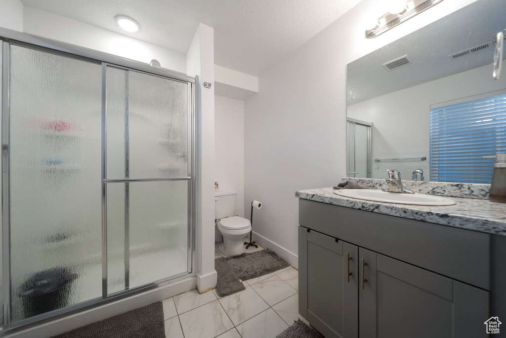 Bathroom featuring vanity, marble look tiles, a shower stall, and toilet