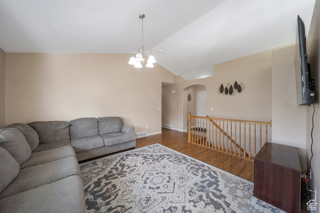 Living area with arched walkways, lofted ceiling, a chandelier, wood finished floors, and baseboards