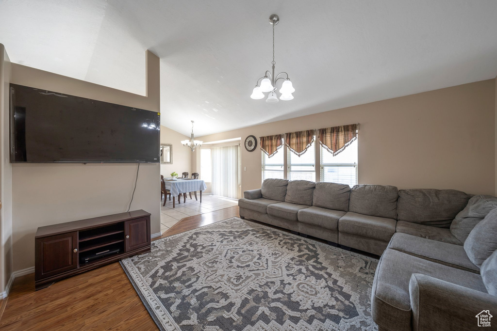 Living room with a chandelier, vaulted ceiling, wood finished floors, and healthy amount of natural light