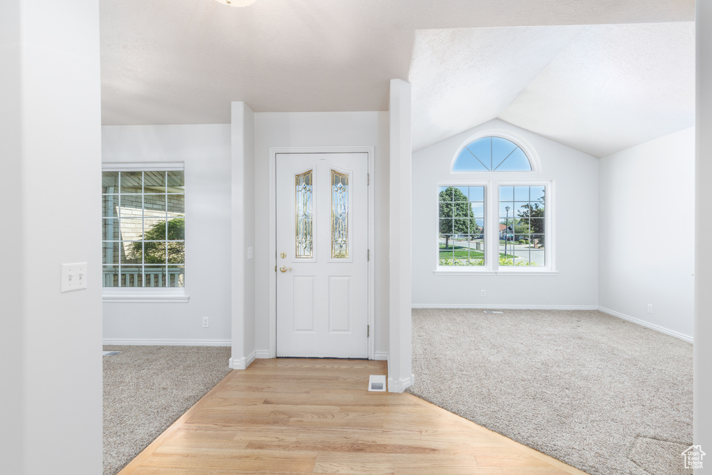 Entrance foyer with light carpet, vaulted ceiling, baseboards, and light wood-type flooring