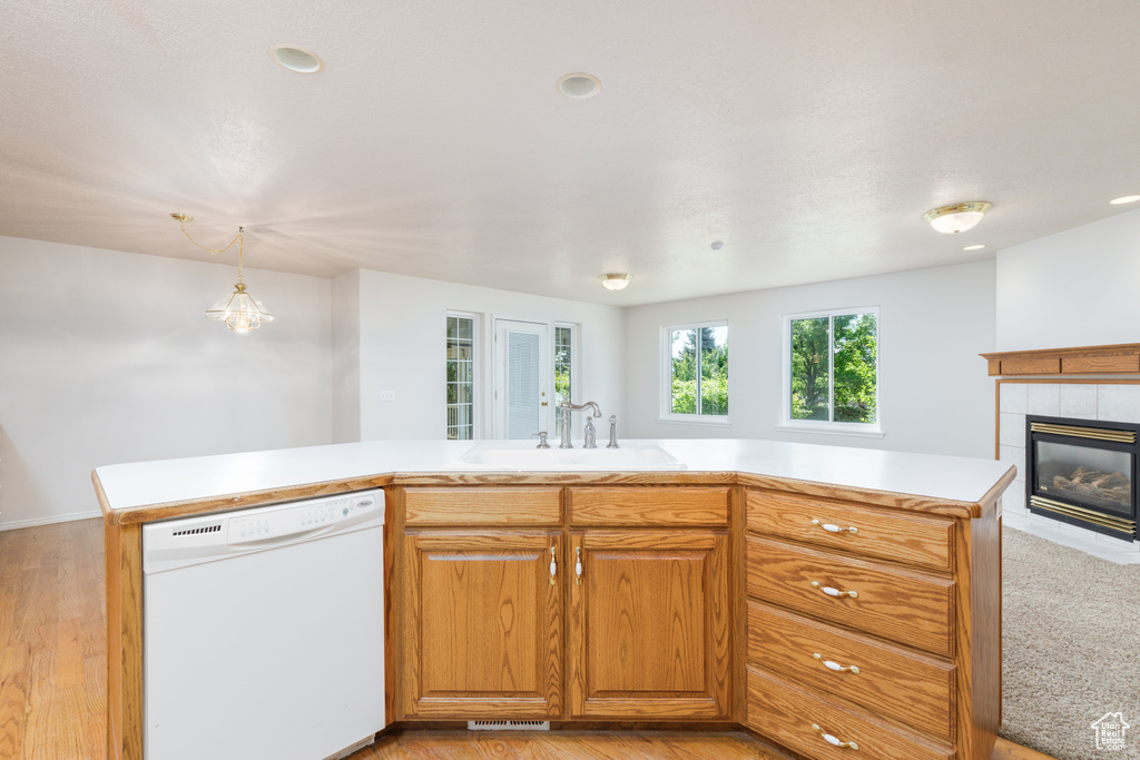 Kitchen with dishwasher, a sink, light countertops, a tile fireplace, and light wood-style floors
