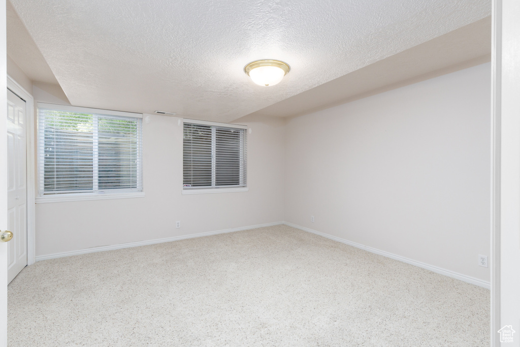 Carpeted empty room with a textured ceiling and baseboards