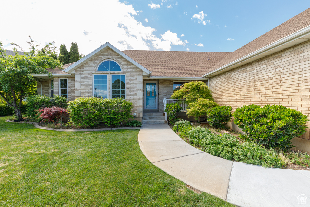 Property entrance with roof with shingles, a yard, and brick siding