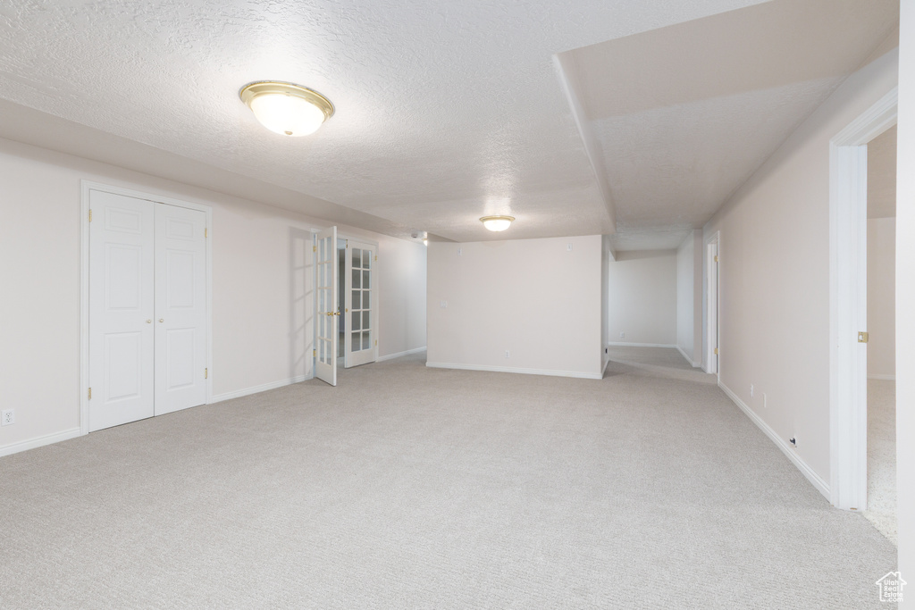 Finished below grade area featuring light carpet, a textured ceiling, and baseboards