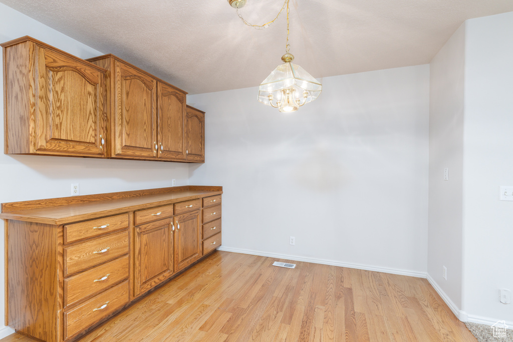 Kitchen with brown cabinetry, light wood-type flooring, a chandelier, baseboards, and decorative light fixtures