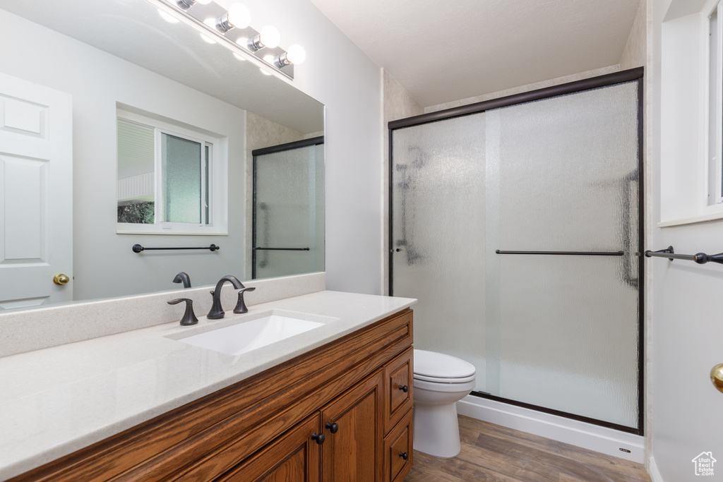 Bathroom featuring wood finished floors, a stall shower, toilet, and vanity