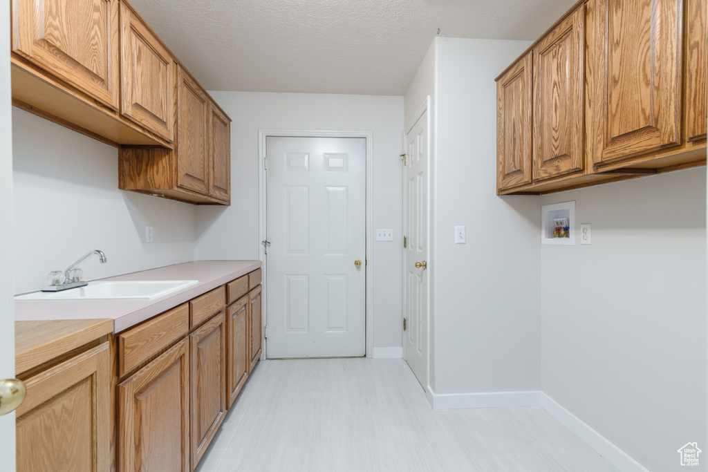 Washroom with cabinet space, washer hookup, baseboards, a textured ceiling, and light floors