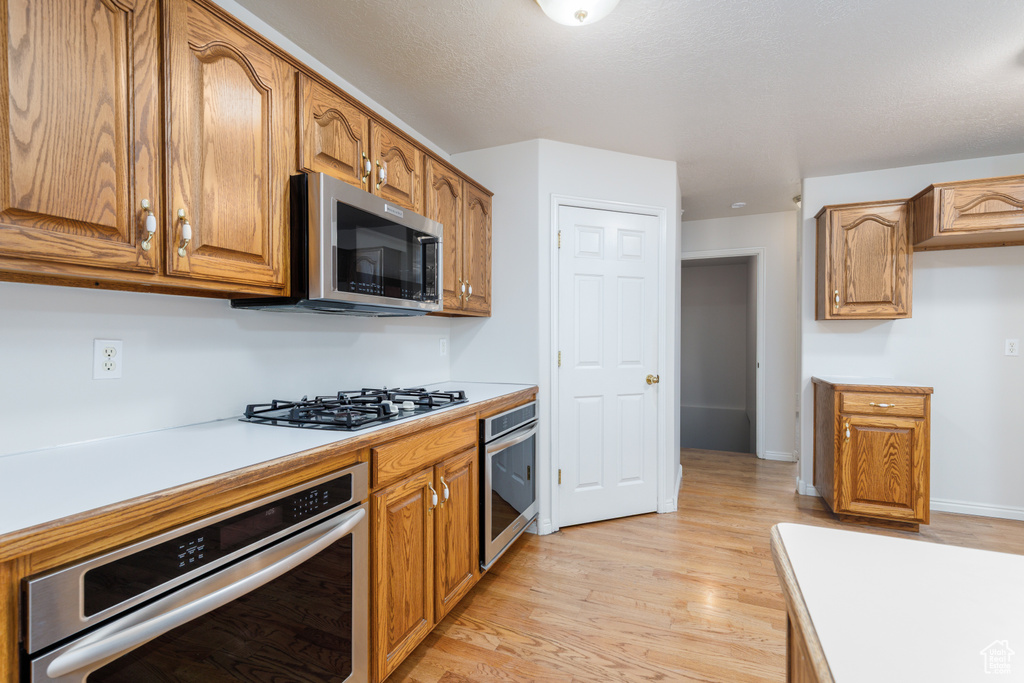 Kitchen with appliances with stainless steel finishes, light countertops, light wood finished floors, brown cabinets, and baseboards
