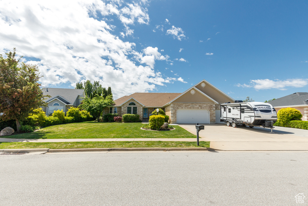 Ranch-style house featuring concrete driveway, an attached garage, a front lawn, and stone siding