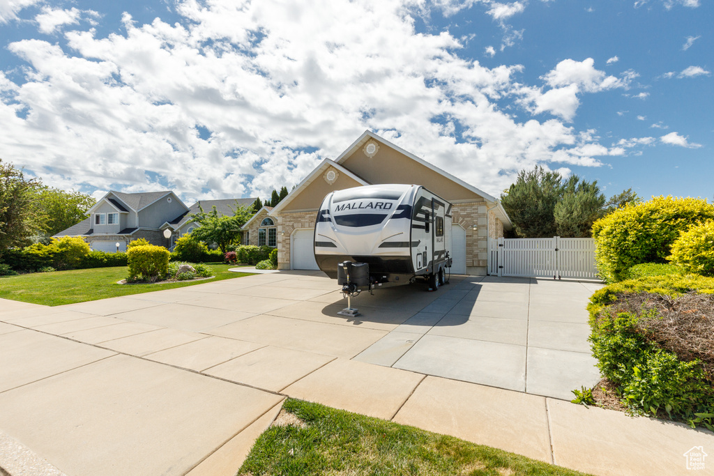 View of front facade featuring a gate, stone siding, concrete driveway, an attached garage, and a front yard