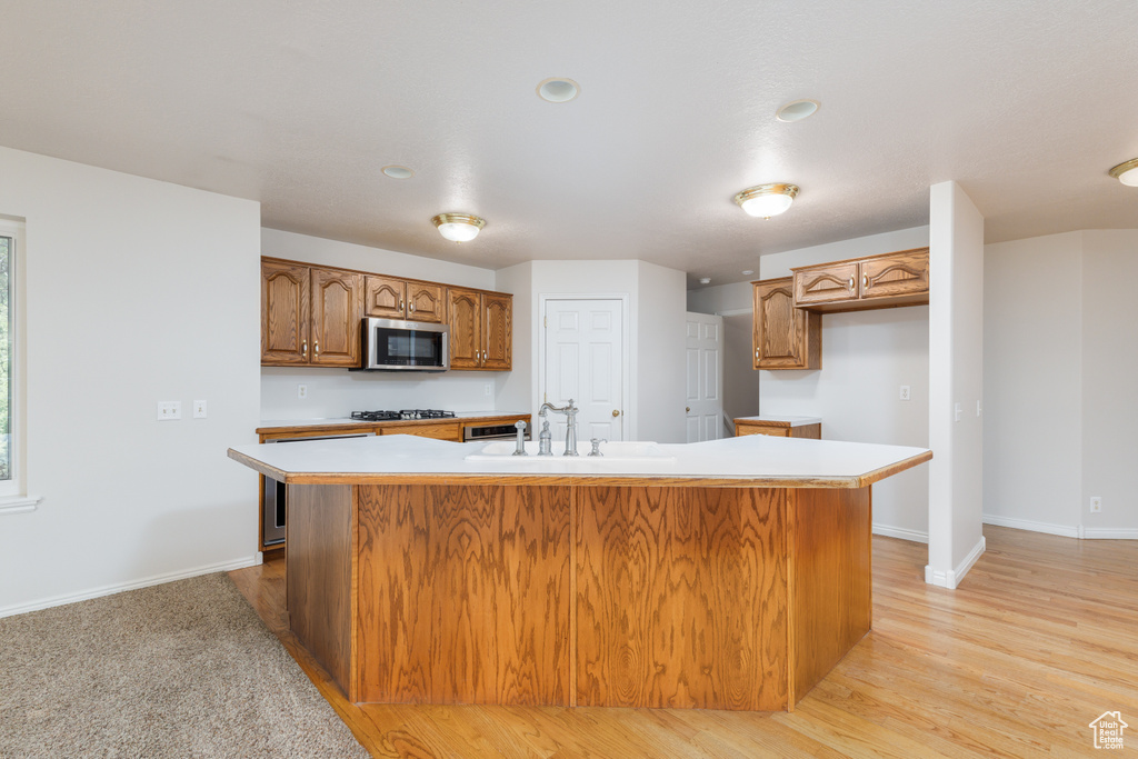 Kitchen featuring stainless steel microwave, a sink, gas cooktop, light countertops, and brown cabinetry