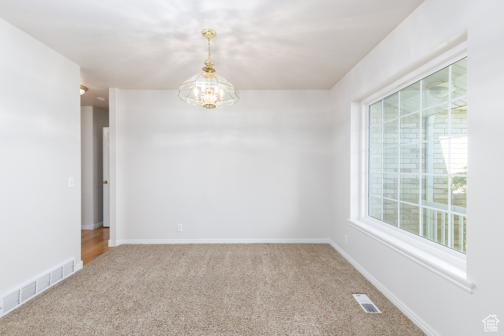 Carpeted empty room with a chandelier and baseboards