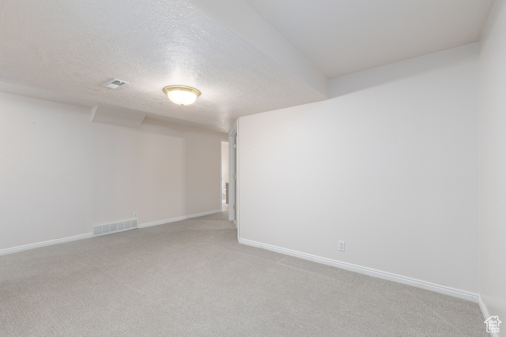 Unfurnished room featuring light carpet, baseboards, and a textured ceiling