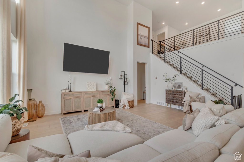 Living area with a towering ceiling, light wood-style floors, recessed lighting, stairs, and baseboards