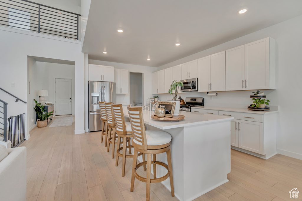 Kitchen with appliances with stainless steel finishes, light wood finished floors, a kitchen bar, white cabinets, and light countertops