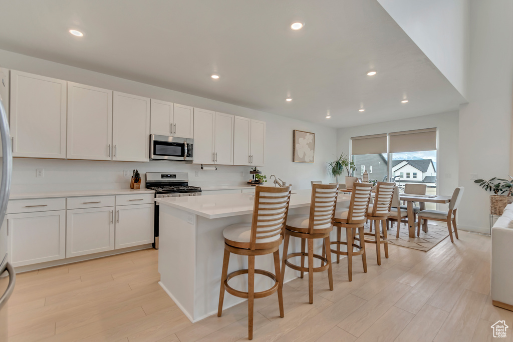 Kitchen with appliances with stainless steel finishes, light countertops, light wood finished floors, white cabinets, and a breakfast bar
