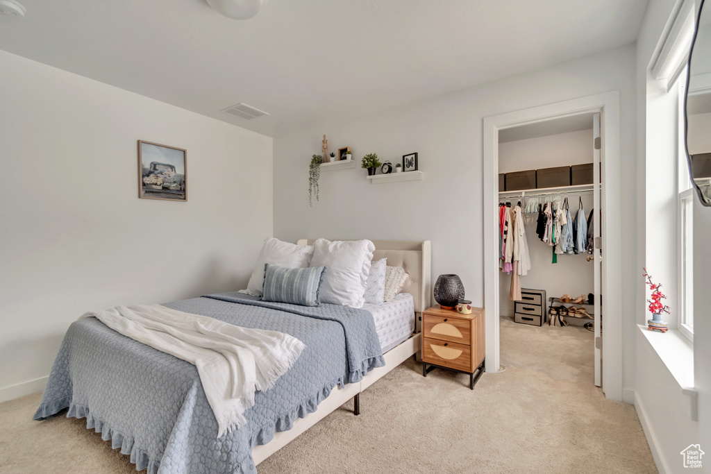 Bedroom with a walk in closet, light carpet, and a closet