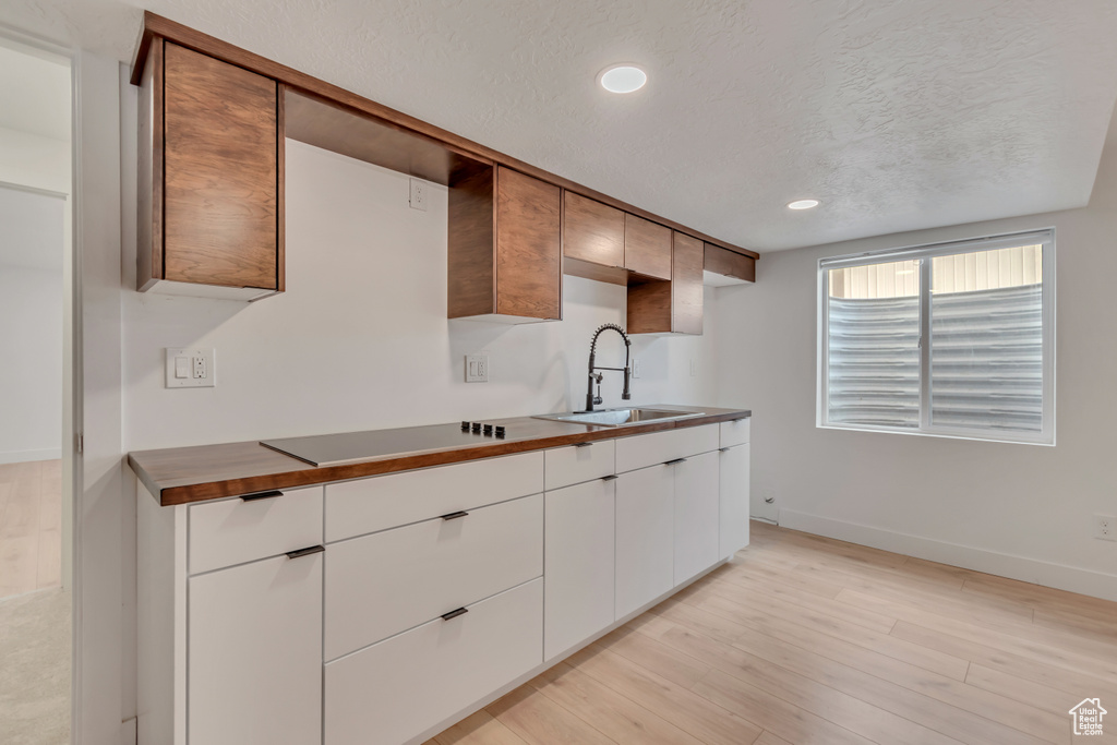 Kitchen featuring a sink, black electric cooktop, baseboards, a textured ceiling, and light wood-type flooring