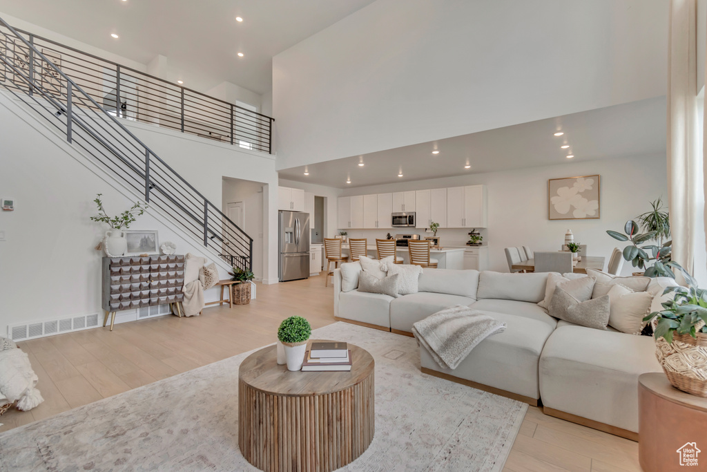 Living room with a towering ceiling, light wood-type flooring, stairway, and recessed lighting