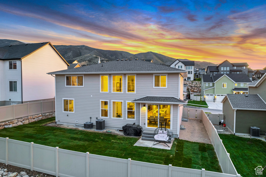Back of property at dusk with central AC, a mountain view, and a patio area