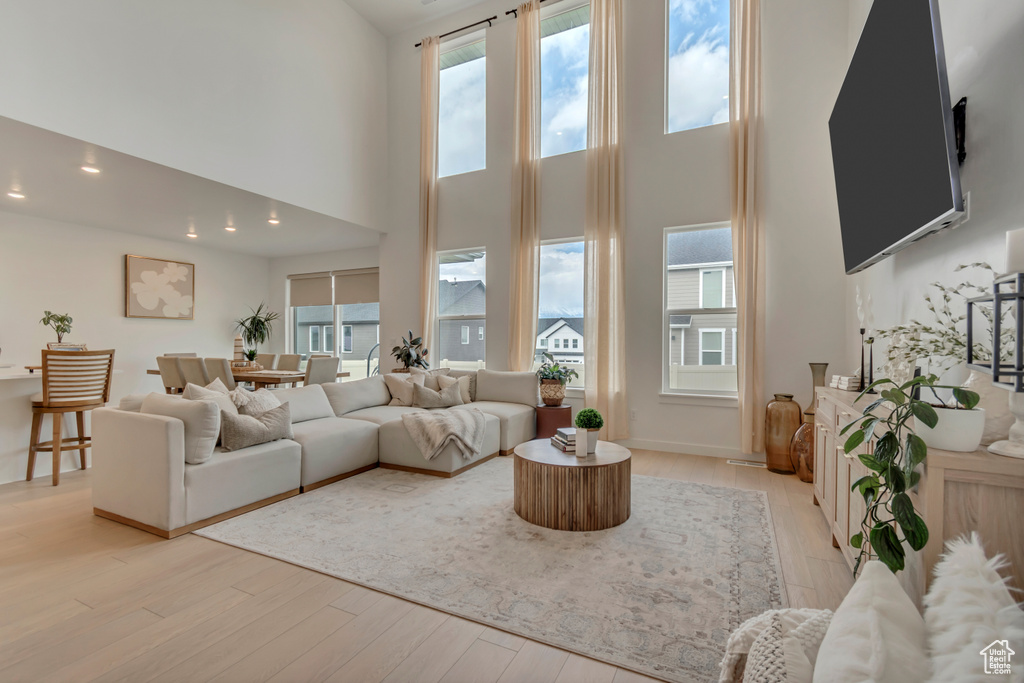 Living room featuring a towering ceiling, light wood-type flooring, healthy amount of natural light, and recessed lighting